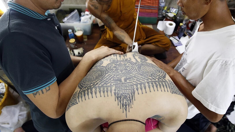 Auf dem traditionellen Tattoo-Fest im Wat-Bang-Phra-Tempel sticht ein buddhistischer Mönch einem Gläubigen mit einem angespitzten Stahlstab ein neues Tattoo.