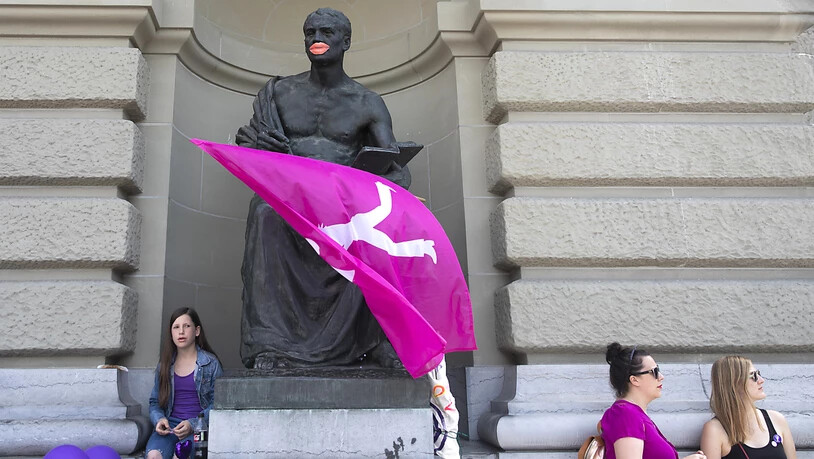 Männliche Statue mit roten Lippen und Fahne am Bundeshaus streikt mit.
