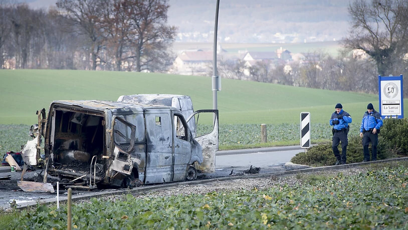 Polizisten begutachten am Tag nach dem Überfall den ausgebrannten Geldtransporter. (KEYSTONE/Laurent Gillieron)