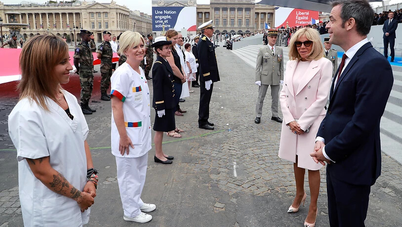Olivier Veran (r), Gesundheitsminister von Frankreich, und Brigitte Macron (2.v.r), Ehefrau von Frankreichs Präsident Macron, reden mit medizinischem Personal am Ende der Militärfeier zum Nationalfeiertag. Foto: Ludovic Marin/AFP/AP/dpa