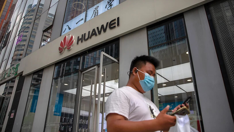 ARCHIV - Ein Mann mit Gesichtsmaske schaut auf sein Smartphone, als er an einem Huawei-Laden in Peking vorbeigeht. Der chinesische Technologiekonzern Huawei soll nun endgültig nicht am Ausbau des superschnellen 5G-Mobilfunknetzes in Großbritannien…
