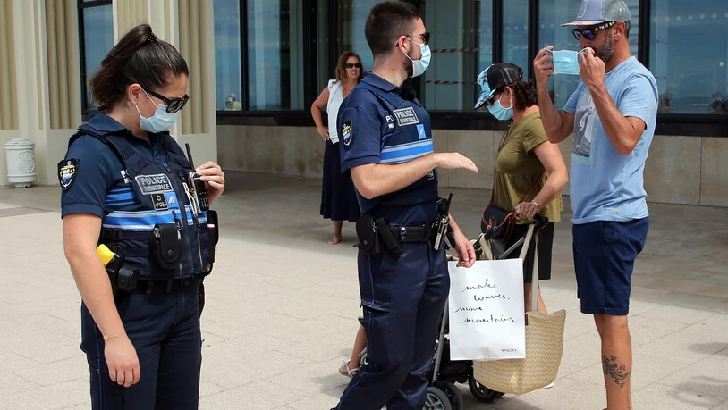 Polizeibeamte weisen Passanten auf das Tragen einer Mund-Nasen-Bedeckung hin. Im Kampf gegen Corona gilt in weiteren französischen Gemeinden jetzt eine Maskenpflicht im Freien. Foto: Bob Edme/AP/dpa