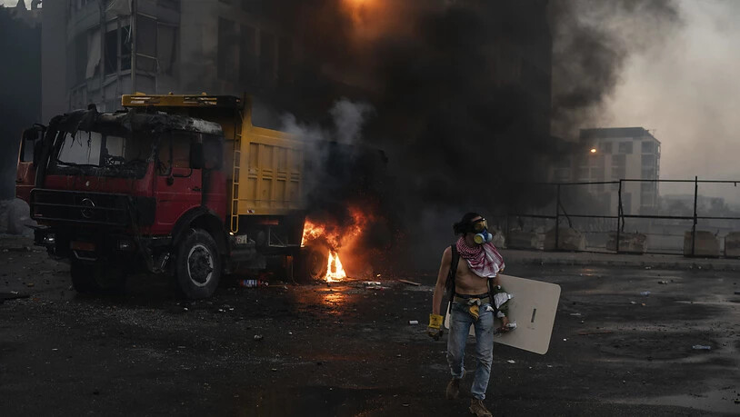 Ein Demonstrant mit Atemmaske und Schutzschild steht vor einem brennenden Lastwagen. Foto: Felipe Dana/AP/dpa