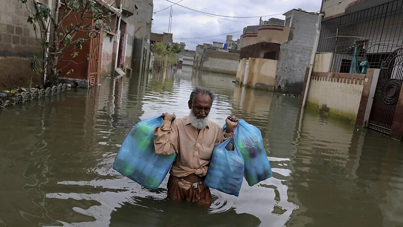Ein Mann trägt Waren, während er nach heftigen Regenfällen durch eine überflutete Straße watet. Nach Überschwemmungen in Pakistans Millionenstadt Karatschi sind in den vergangenen drei Tagen mindestens 41 Menschen ums Leben gekommen. Foto: Fareed Khan/AP…