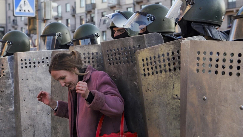 Eine Frau steht bei einer Kundgebung der Opposition, um gegen die offiziellen Ergebnisse der Präsidentschaftswahlen zu protestieren, vor Polizisten mit Schilden. Foto: Uncredited/AP/dpa