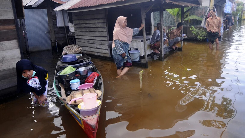 Anwohner stehen auf der überfluteten Straße vor ihren Häusern auf der indonesischen Insel Borneo. Foto: Iman Satria/AP/dpa