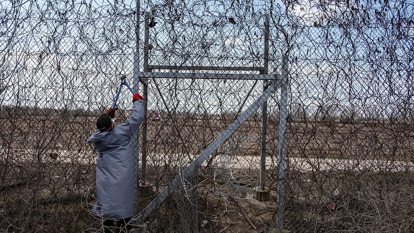 ARCHIV - Ein Migrant steht am Grenzzaun an der türkisch-griechischen Grenze und versucht, mit einer Drahtschere den Zaun durchzuschneiden. Foto: Yasin Akgul/dpa
