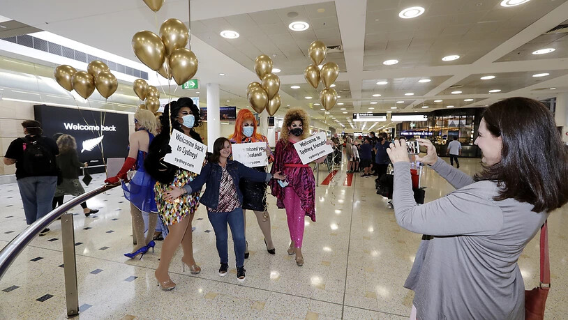 Eine Passagierin aus Neuseeland (M) stellt sich mit sich für ein Foto mit Drag Queens, die sie am Flughafen Sydney begrüßen, auf. Erstmals seit Beginn der Corona-Pandemie können Menschen in Neuseeland und Australien ab dem 19. April wieder zwischen…
