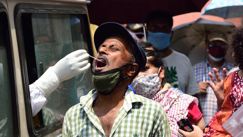 Ein Mitarbeiter des indischen Gesundheitswesens sitzt in einem Auto und entnimmt durch das Fenster einem Mann für einen Corona-Test einen Abstrich. Foto: Sumit Sanyal/SOPA Images via ZUMA Wire/dpa
