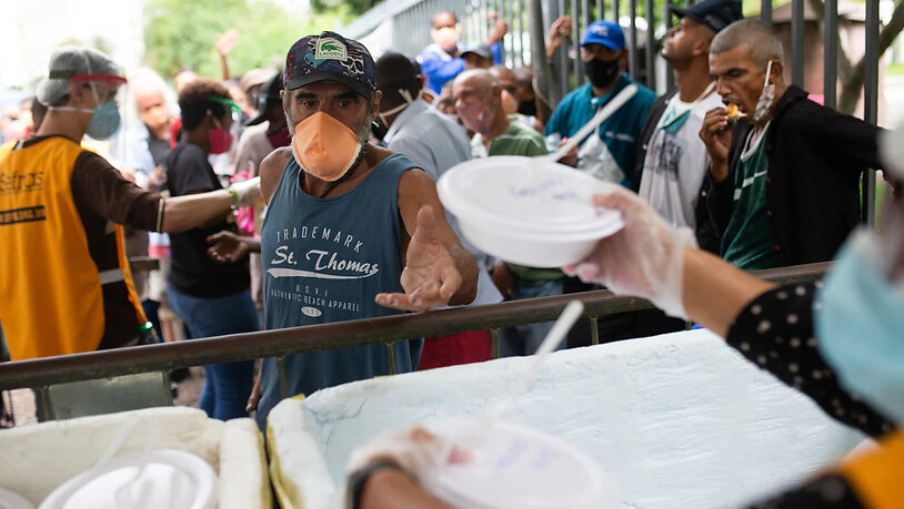 Zahlreiche Menschen stehen für eine Mahlzeit an, die von Freiwilliger der franziskanISCHE Initiative namens Sefras inmitten der Corona-Pandemie ausgegeben werden. Foto: Fernando Souza/dpa