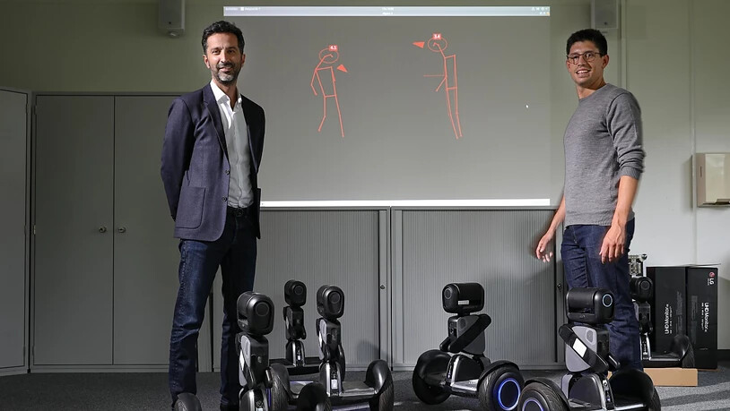 Laborleiter Alexandre Alahi (links) und Doktorand Lorenzo Bertoni (rechts) im Visual Intelligence for Transportation Laboratory an der ETH Lausanne EPFL. Auf der Leinwand hinter ihnen Strichmännchen, zu denen die Abstands-Analysanden umgewandelt werden  …