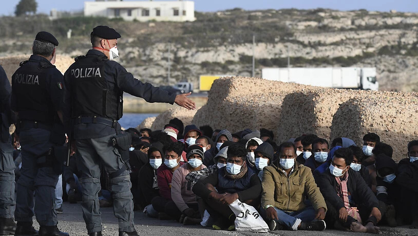 dpatopbilder - Italienische Polizisten  und eine Gruppe Migranten:. Auf der kleinen italienischen Mittelmeerinsel Lampedusa sind innerhalb kurzer Zeit mehr als 2000 Bootsmigranten angekommen. Foto: Salvatore Cavalli/AP/dpa