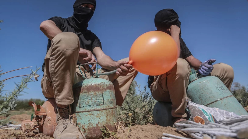 Maskierte Palästinenser füllen in einem Gebiet östlich von Gaza-Stadt Ballons mit Kühlgas, die dann mit Brandsätzen und brennbarem Material versehen werden und vom Wind in israelisches Gebiet getragen werden sollen. Foto: Mohammed Talatene/dpa