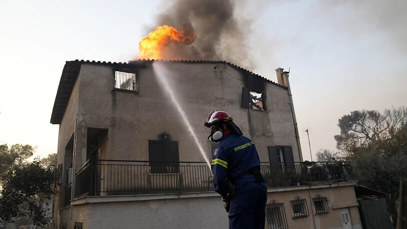 Ein Feuerwehrmann löscht einen Brand an einem Gebäude, der durch das Feuer von Waldbrände entfacht ist. Feuerwehrleute in Griechenland kämpfen auch am Mittwochmorgen weiter gegen den Großbrand in den nördlichen Vorstädten Athens. Regierungschef Kyriakos…