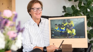 Zwei Welten: Rosina Hug präsentiert den All-In-One Low-Power-Computer mit einem hölzernen Rahmen. Auf dem Bildschirm zu sehen sind afrikanische Schüler, die sich um einen Computer versammeln.